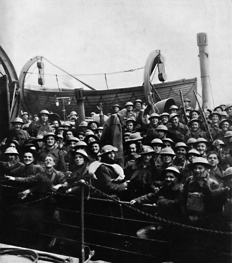 A black and white photo of British soldiers being evacuated from Dunkirk. They are tightly packed onto a ship and many are smiling and waving to the camera.