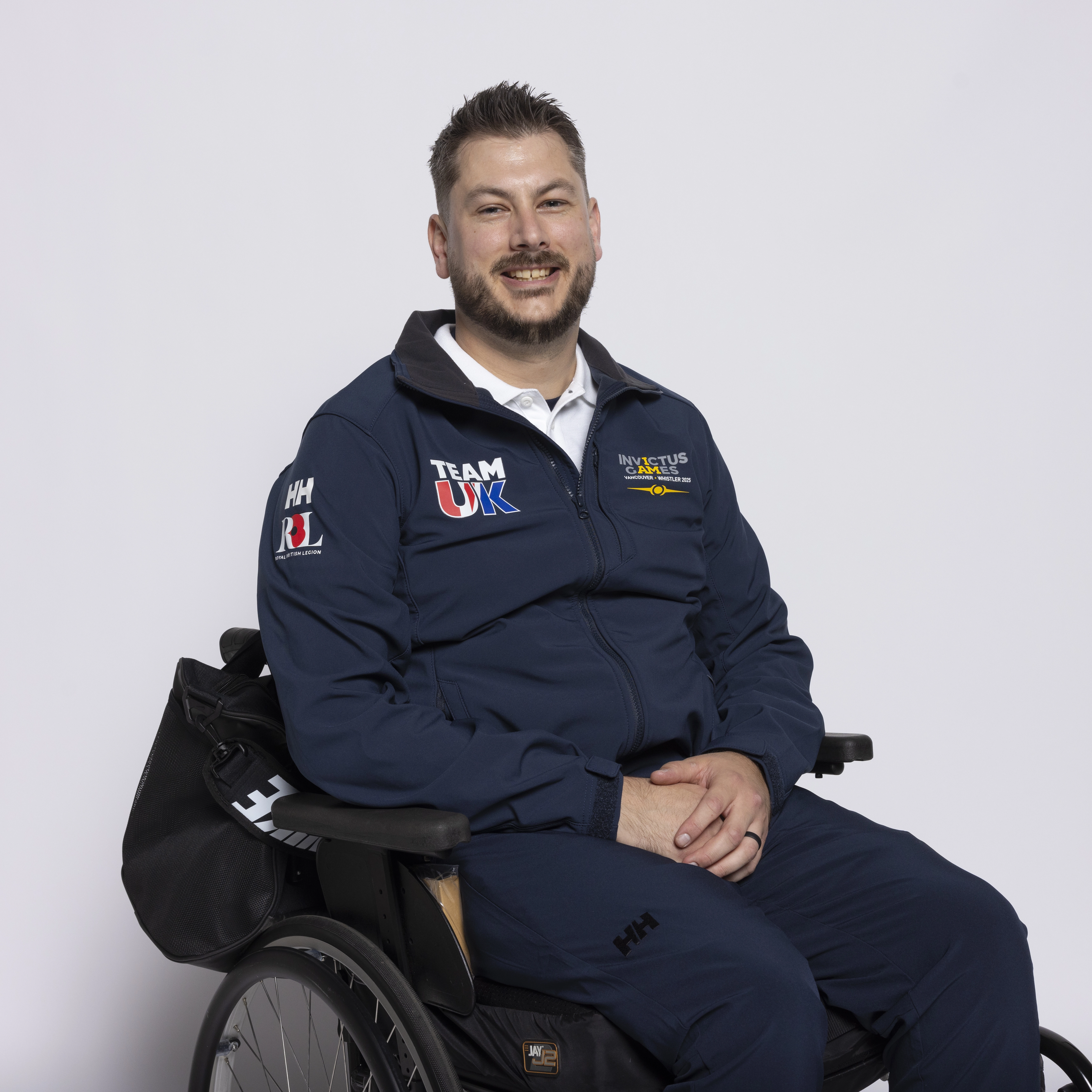 Neil sits in a wheelchair smiling at the camera whilst wearing a navy blue Invictus Games kit.
