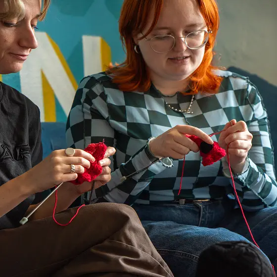 A participant knitting a red poppy flower for a crafting campaign.