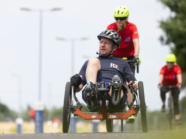 RBL_Invictus_Training_Camp-60 Al in a recumbent bike on a racing track. Behind him we can see another RBL competitor on a different adaptive bike. They are both wearing helmets and RBL t-shirts.