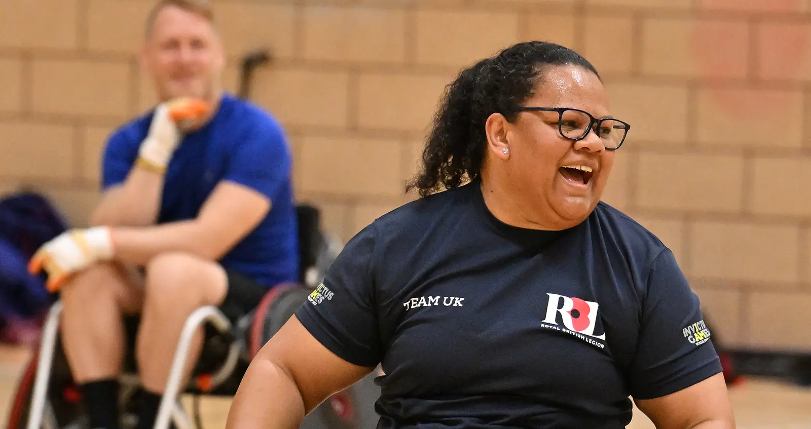 A woman photographed in motion in a wheelchair during a wheelchair basketball game. She is wearing a navy t-shirt that has the RBL logo on one side and Team UK written on the other side, and black shorts and white trainers.