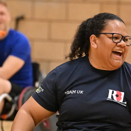 A woman photographed in motion in a wheelchair during a wheelchair basketball game. She is wearing a navy t-shirt that has the RBL logo on one side and Team UK written on the other side, and black shorts and white trainers.