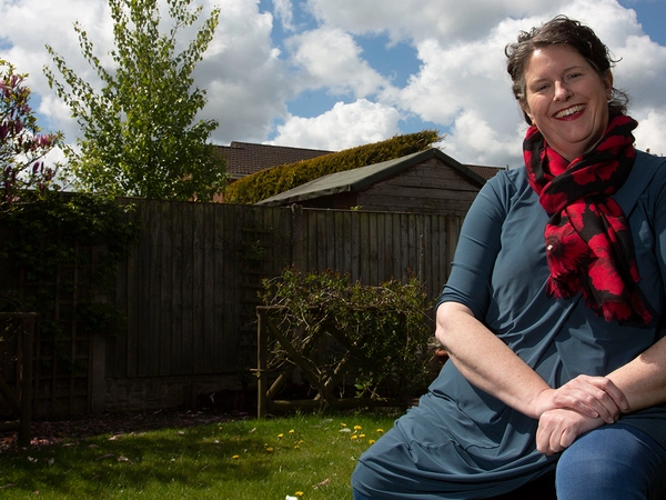 Nicola Cook 2 Woman sat outside on bench smiling