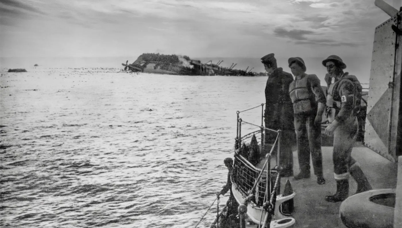 HMT Lancastria A black and white photo of 3 uniformed men standing on the deck of a rescue ship, watching the sinking HMT Lancastria. The Lancastria has capsized and is partially submerged. Its propeller is visible above water. Debris is floating in the water nearby.