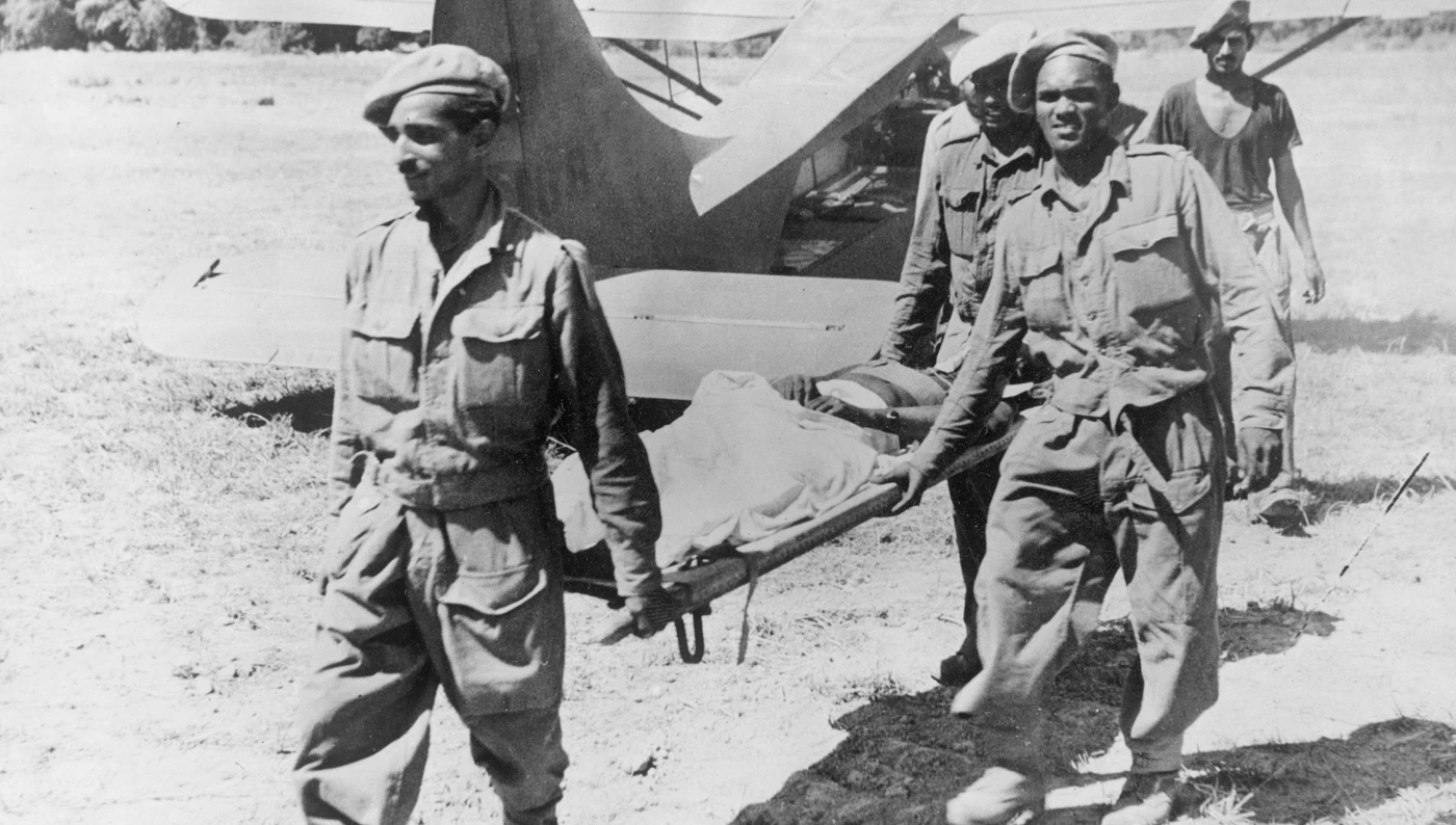 A wounded West African soldier is carried on a stretcher by soldiers after fighting in Burma