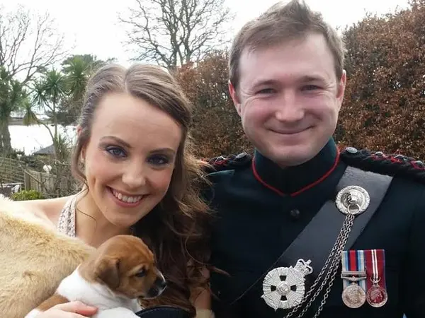 Victoria holding a puppy and standing with her husband.