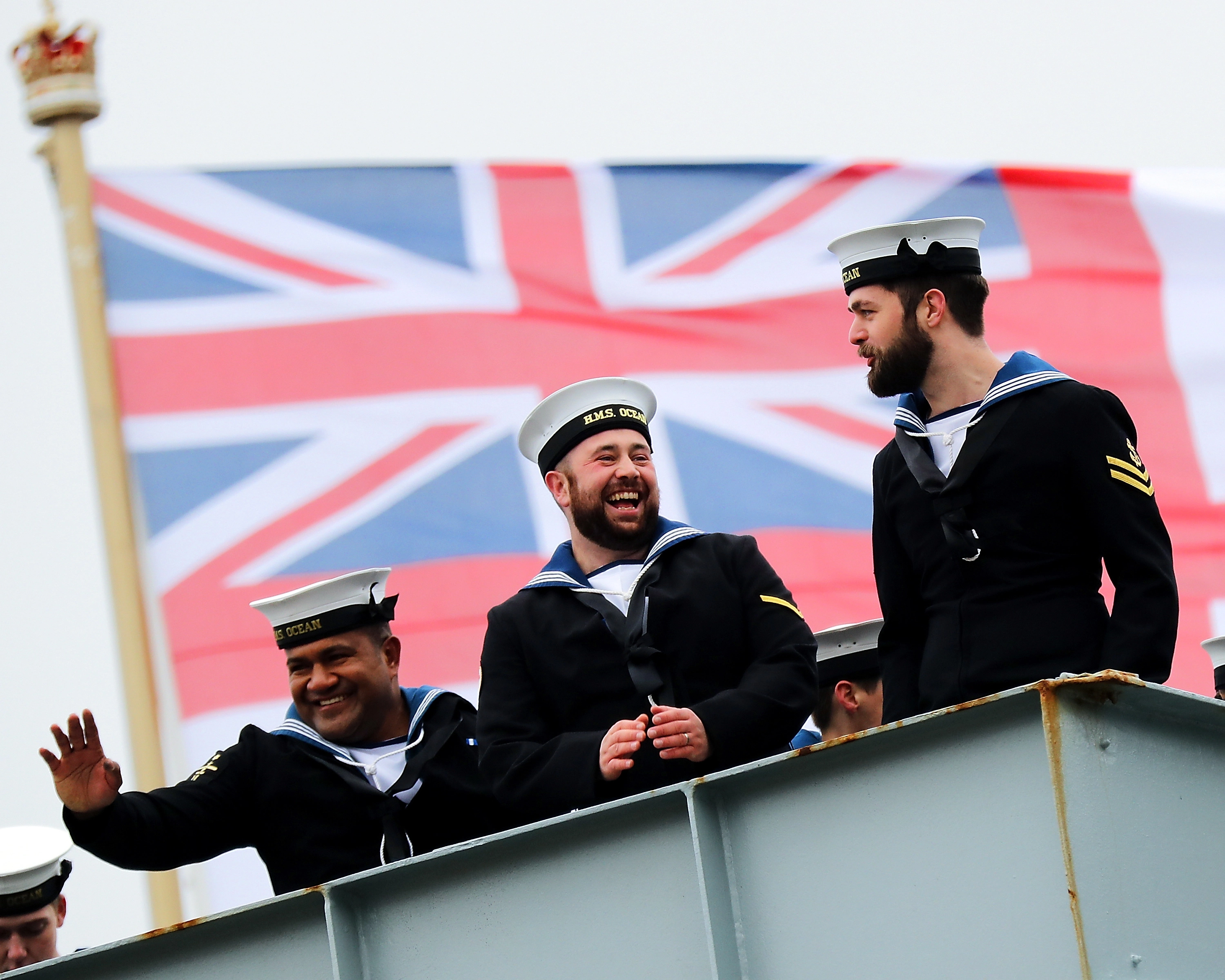 Personnel from the Royal Navy waving in front of a union jack