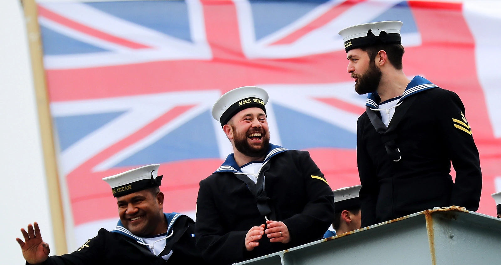 Personnel from the Royal Navy waving in front of a union jack