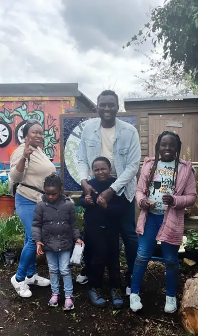 Emmanuel is photographed with his family - his wife adn their three children. They are all smiling for the picture and standing in a relaxed manner.