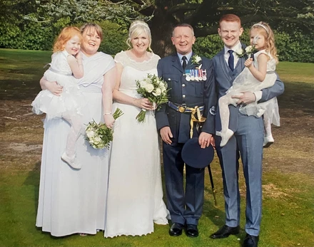 Emilia, Leanne, Gina, Al, Rob & Esme Dyer Al and Gina on their wedding day. They are standing in between relatives who are holding two young girls in their arms.
