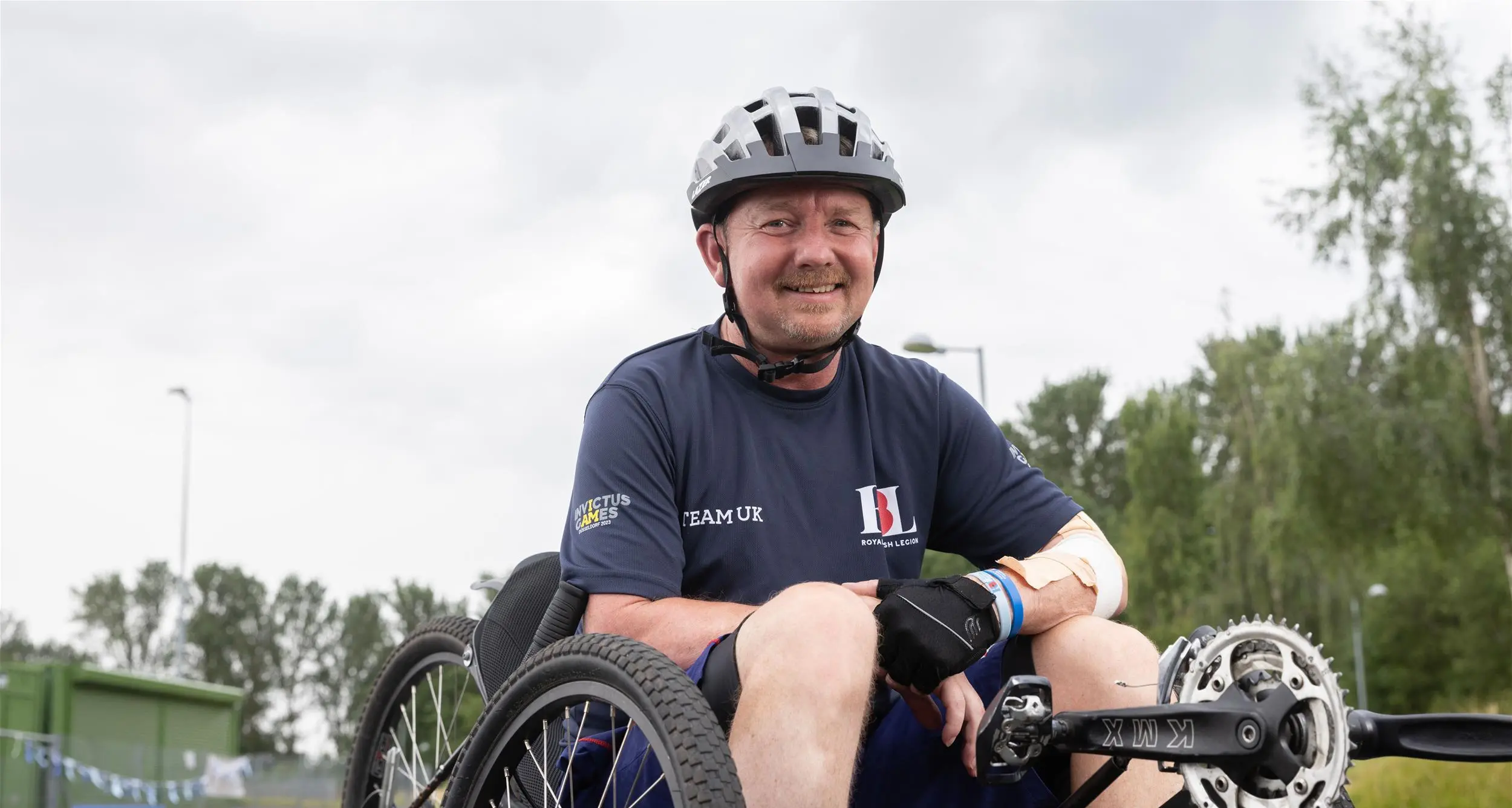 Al sat in a recumbent bike on a racing track. He is in a resting position with his hands propped on his legs.He is wearing a navy RBL Team UK t-shirt and has a helmet on.