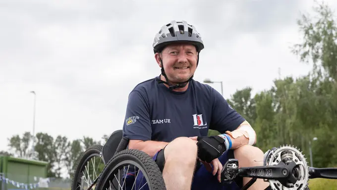 RBL_Invictus_Training_Camp-31 Al sat in a recumbent bike on a racing track. He is in a resting position with his hands propped on his legs.He is wearing a navy RBL Team UK t-shirt and has a helmet on.