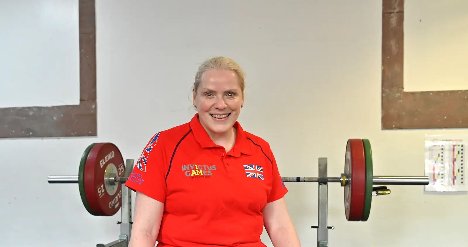 Amanda in a red Invictus Games Team UK polo shirt. There is a barbell with weights on it behind her.