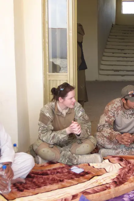 Photo of Amanda in combat gear. She is sat on some blankets on crossed legs. We can see some people also dressed in combat gear sat to either side of her.