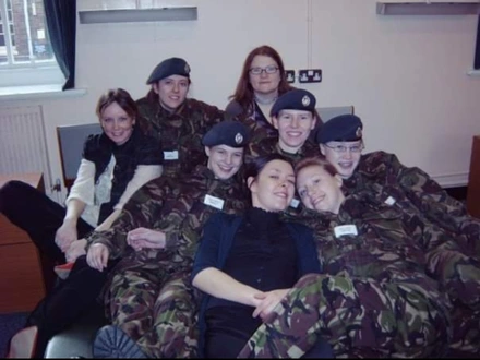 Liz in a group of other young Armed Forces personnel. They are all dressed in combat gear and are huddled together on the floor to take the picture.