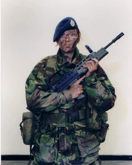 Liz in full combat gear. She has paints smeared over her face and is holding a gun.