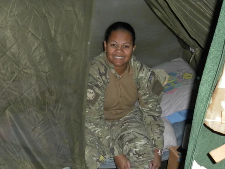 Tilly in service Tilly is smiling at the camera. She is wearing combat clothes. She appears to be sitting on a makeshift bed inside a green tent.