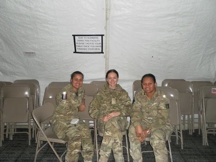 Tilly on the left Tilly sat on chairs with two friends to her right. They are all sat on chairs inside what looks like a white tent, wearing combat gear.