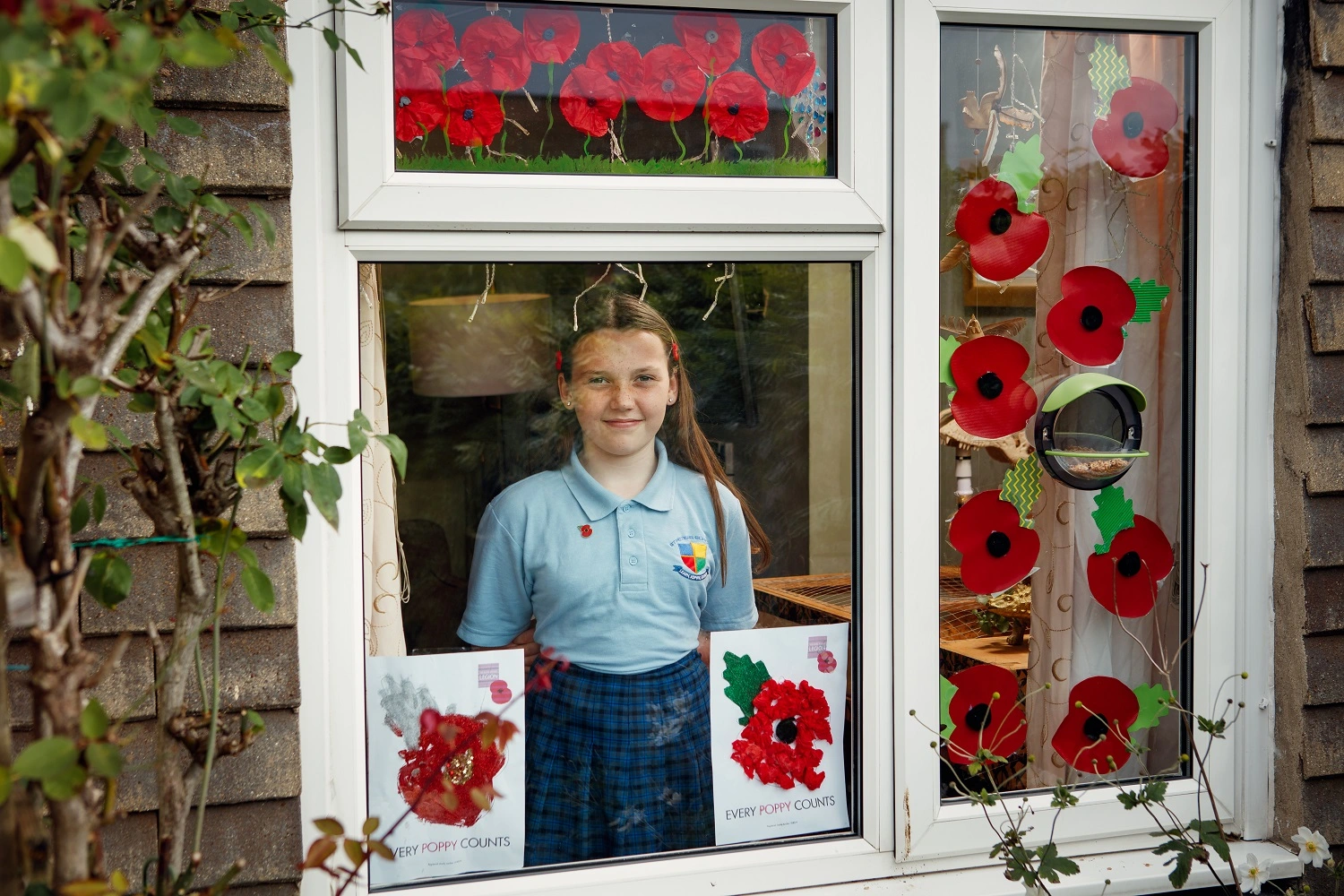 Poppy Railton at her window with poppy posters she has decorated