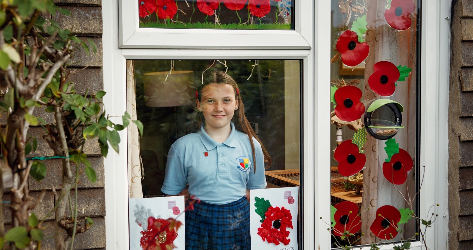 Poppy Railton at her window with poppy posters she has decorated