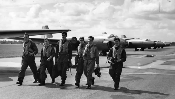 Black and white photograph of National Service aircrew walking through an airfield past a Canberra jet.
