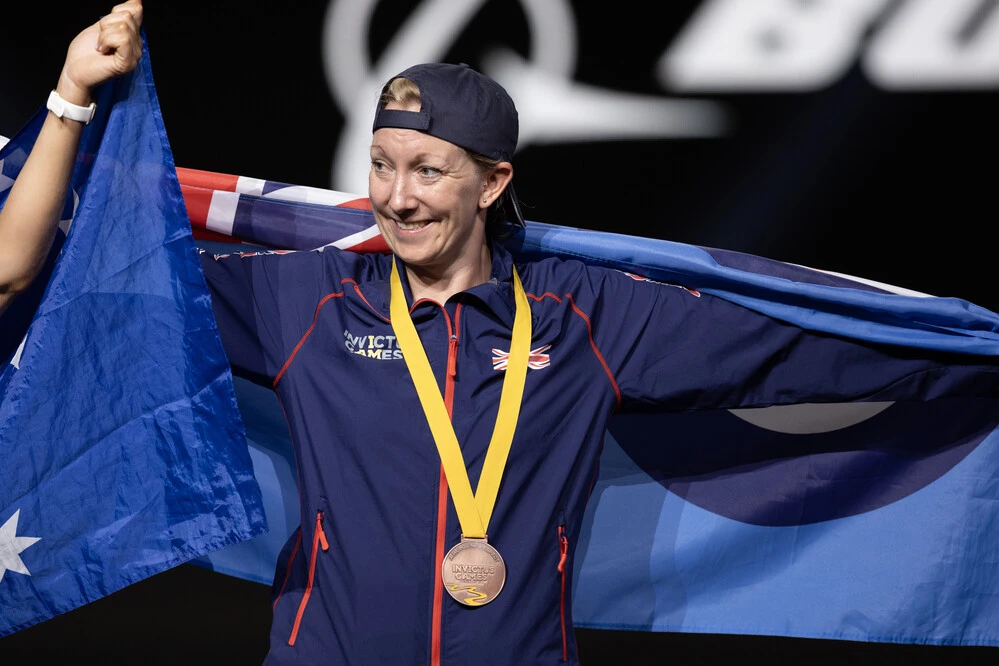 Stacey Denyer at Invictus Games 2023 celebrating her Bronze medal with a British flag.