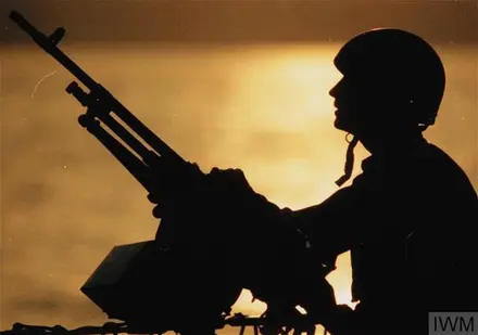 A Royal Marine mans a Machine Gun on board HMS BRAVE at sunset in the Gulf