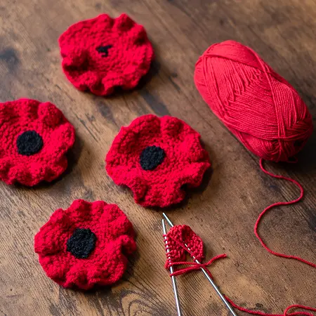 Handmade red knitted poppies resting on a wooden tabletop.